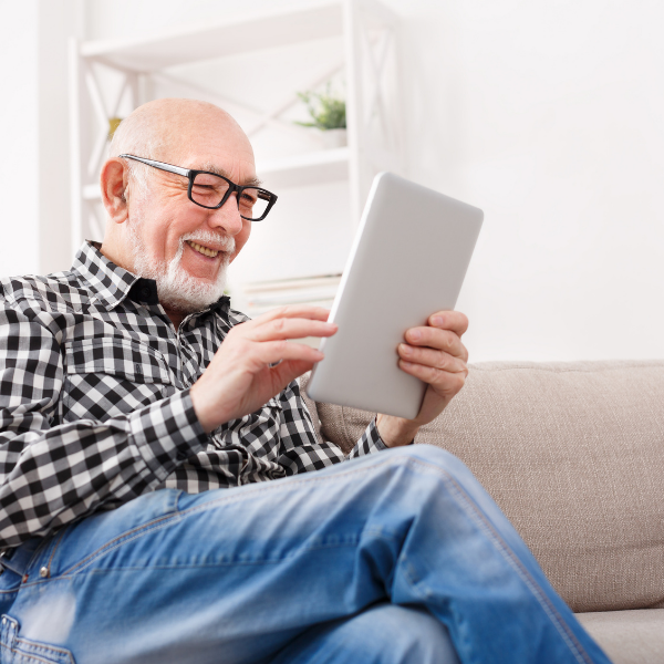 Photo of an older white man smiling while looking at an iPad like device