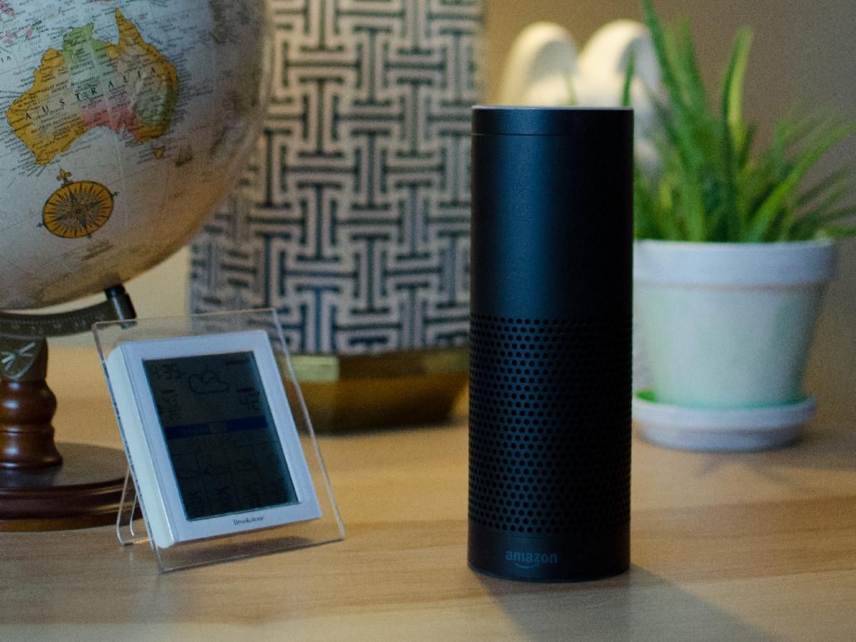 Amazon Alexa on a table with a lamp a globe and a potted plant.